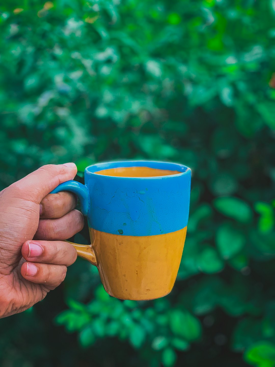 Una mano tiene una tazza blu e gialla piena di caffè.