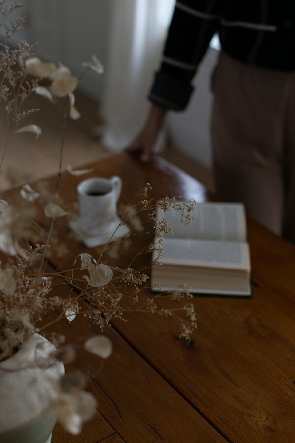 Mano appoggiata su un tavolo di legno con un libro e un caffè.